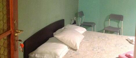 Un dormitorio con cama, dos sillas, una mesita de noche y dos cuadros en la pared.