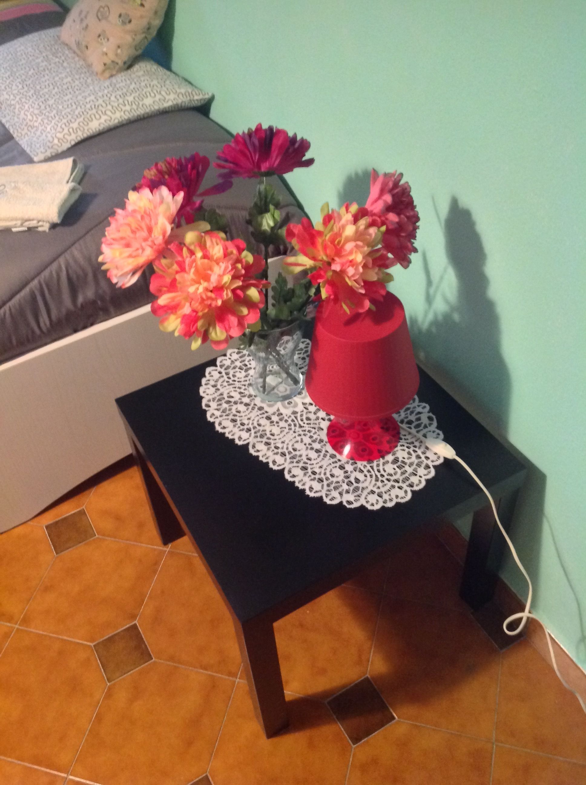 Una pequeña mesa negra con un mantel de encaje y un florero rojo con flores.