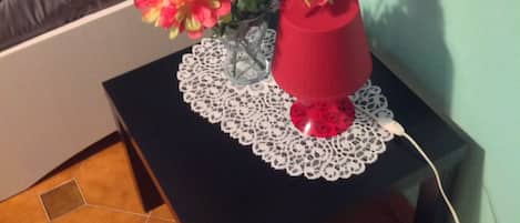 Una pequeña mesa negra con un mantel de encaje y un florero rojo con flores.