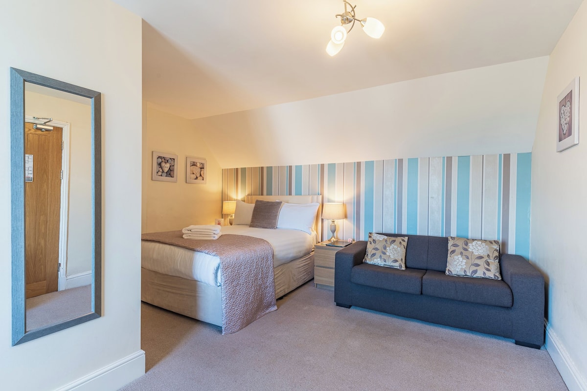A bedroom with a bed, bedside table, lamp, and a sofa.
