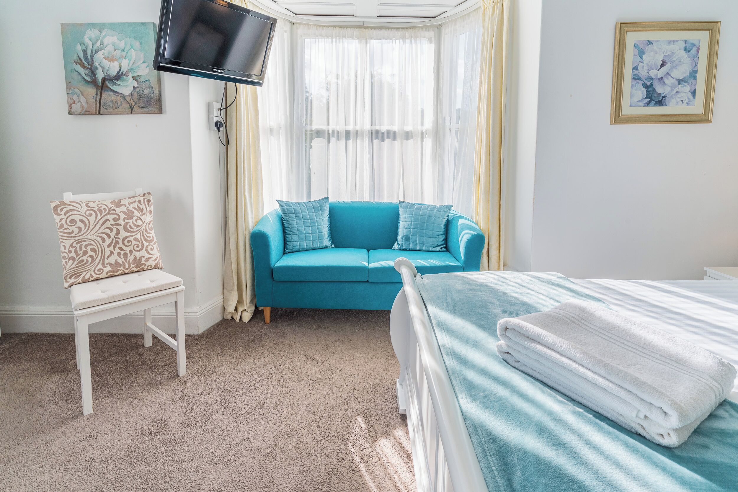 Ein Schlafzimmer mit einem Bett, einem blauen Sofa, einem weißen Stuhl und einem an der Wand befestigten Fernseher.