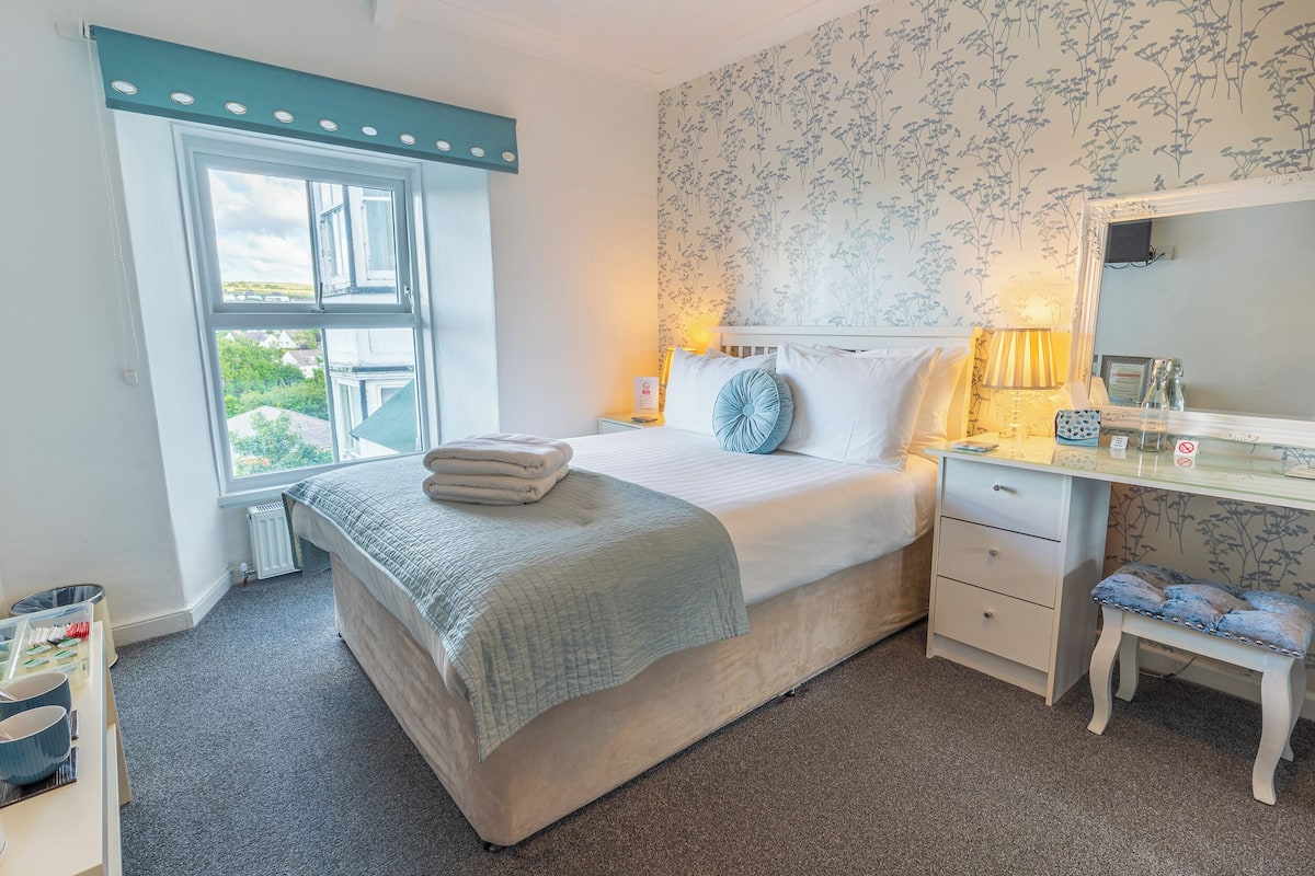 A neatly arranged bedroom with a bed, bedside tables, a desk, and a chair.