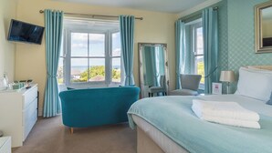 A hotel room with a bed, a desk, a chair, a TV, and a window with curtains. - Rooms at The Highcliffe (Cardigan)