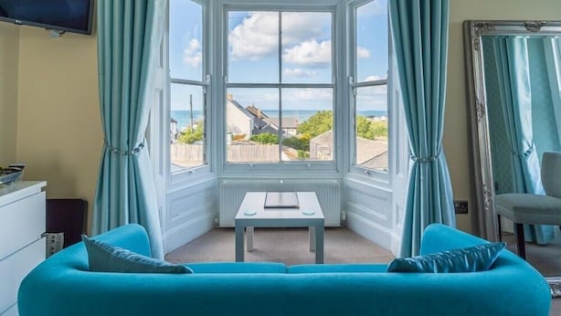 A room with a bay window, a sofa, a table, and a chair. - Rooms at The Highcliffe (Cardigan)