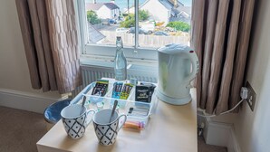 A table with mugs, a kettle, and a tray of snacks by a window overlooking a coastal view. - Rooms at The Highcliffe (Cardigan)