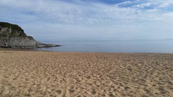 Una playa arenosa con un acantilado rocoso a la izquierda y un mar tranquilo al fondo.