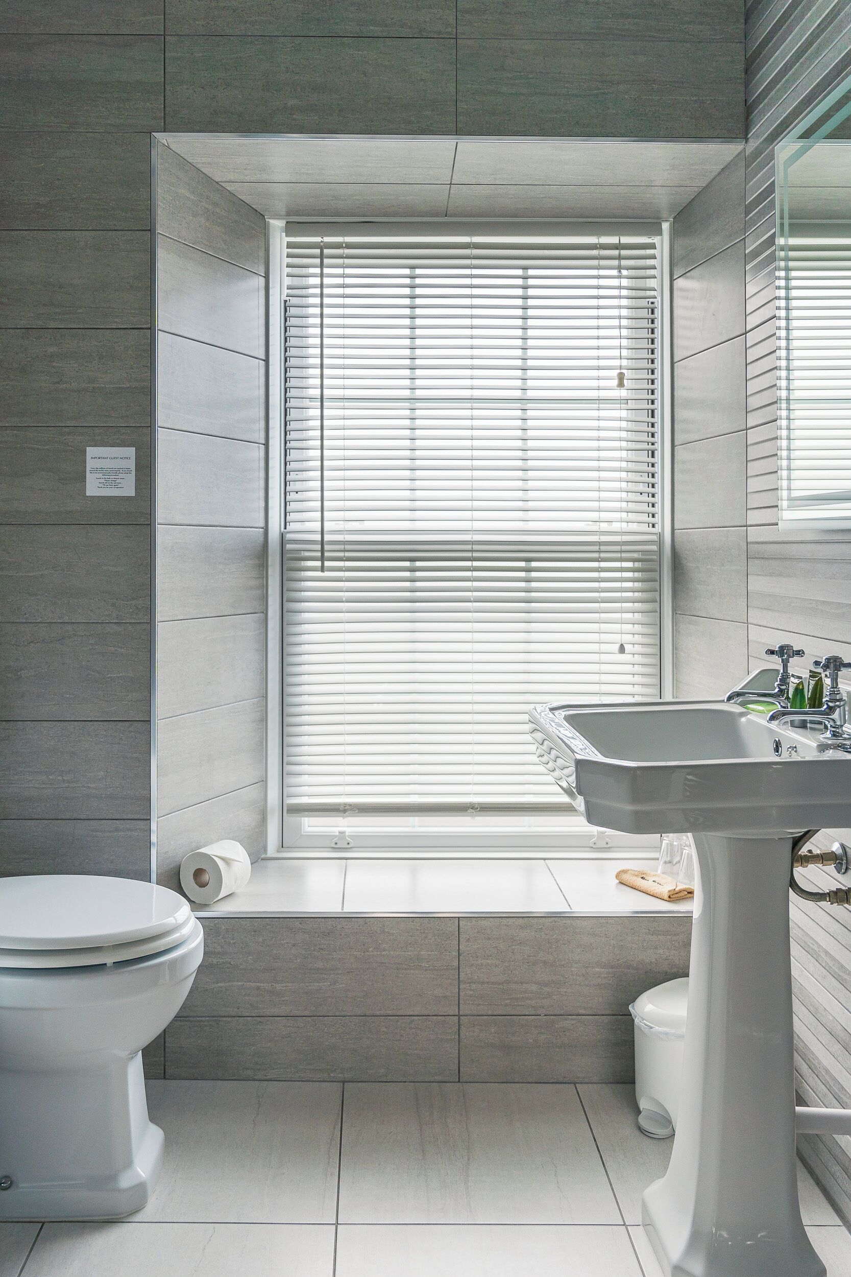 A bathroom with a toilet, sink, and window with blinds.