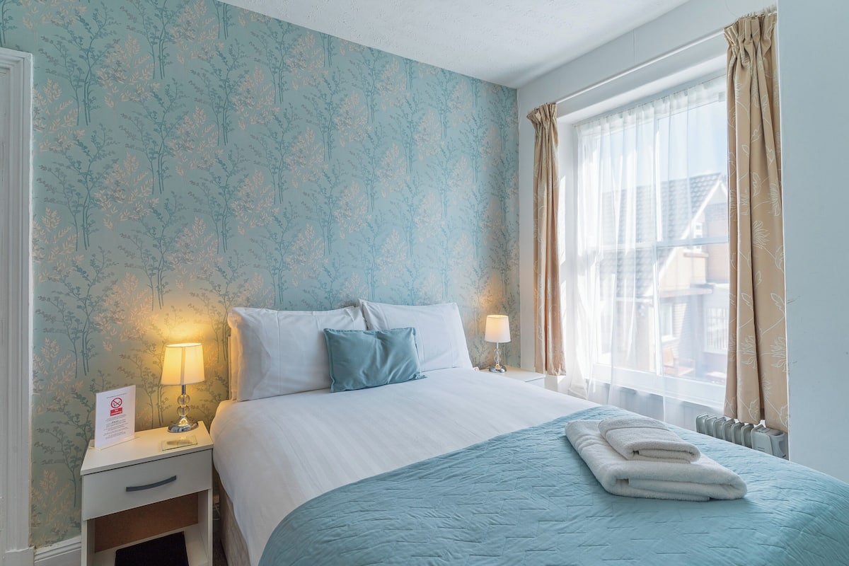 A hotel room with a bed, nightstands, a sign, and a window with curtains.