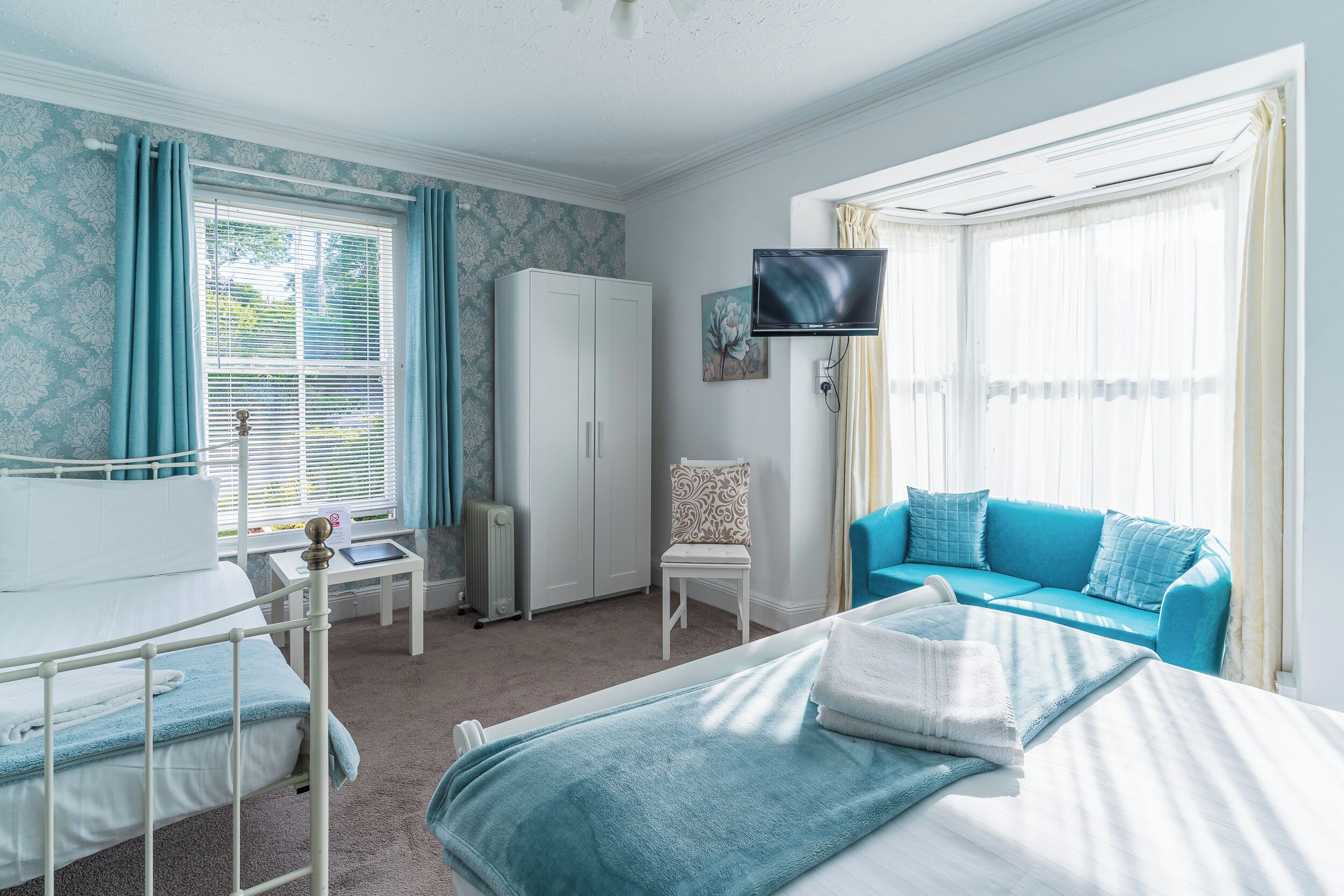 A bedroom with a bed, a chair, a sofa, a TV, and a wardrobe.