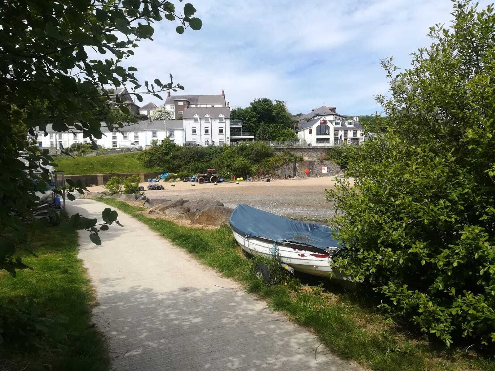A coastal pathway with a boat, a tractor, and buildings in the background.