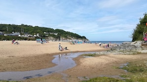 A beach with people, a rocky area, and a clear sky. - Rooms at The Highcliffe (Cardigan)