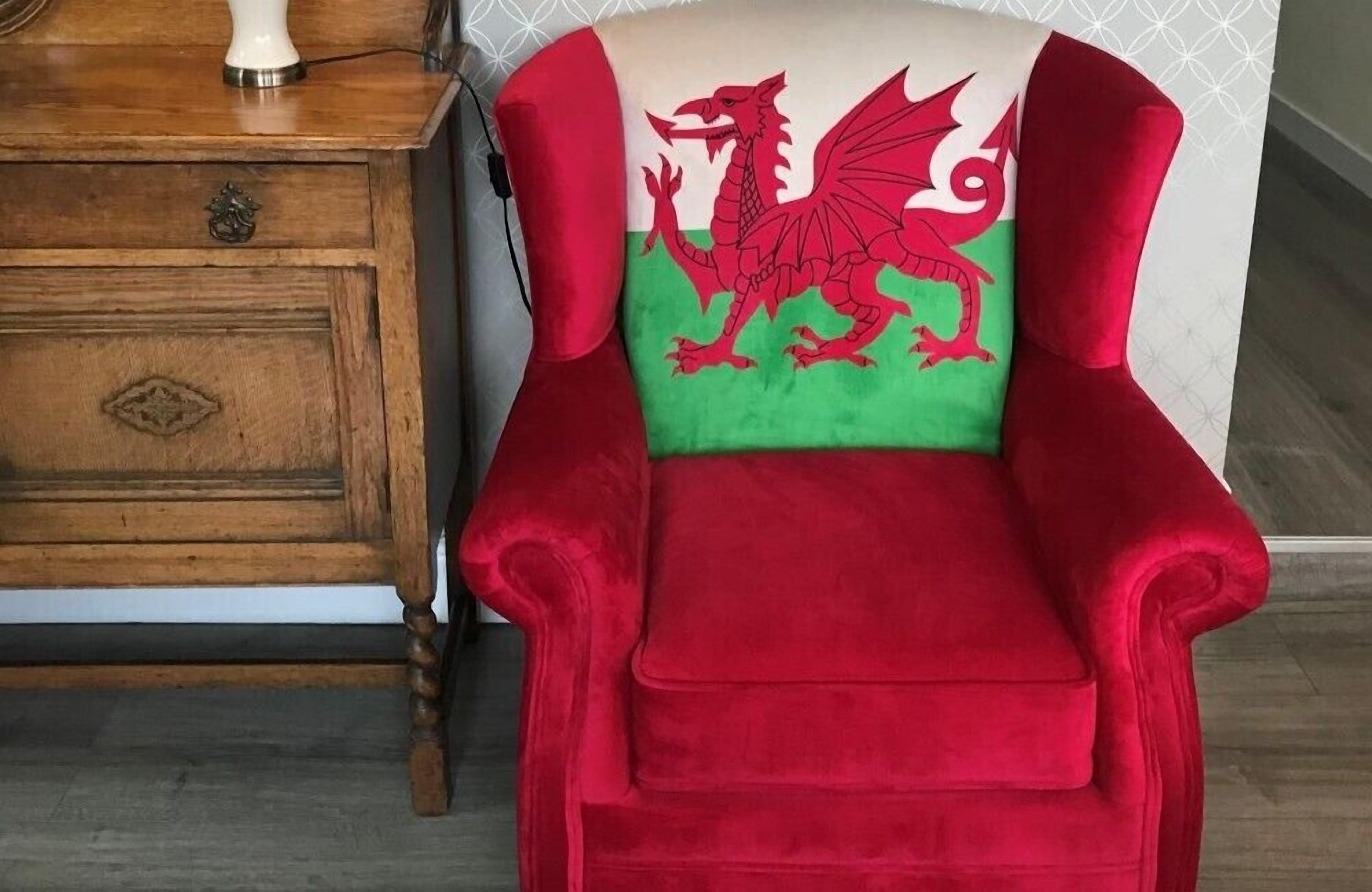 Una poltrona rossa con un motivo a drago sullo schienale, posizionata accanto a un comodino in legno con un cassetto e una lampada.