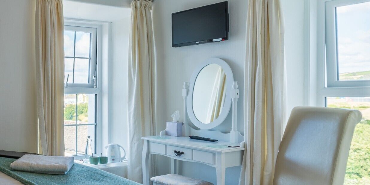 A hotel room with a bed, a desk with a mirror, a television, and a window with curtains.