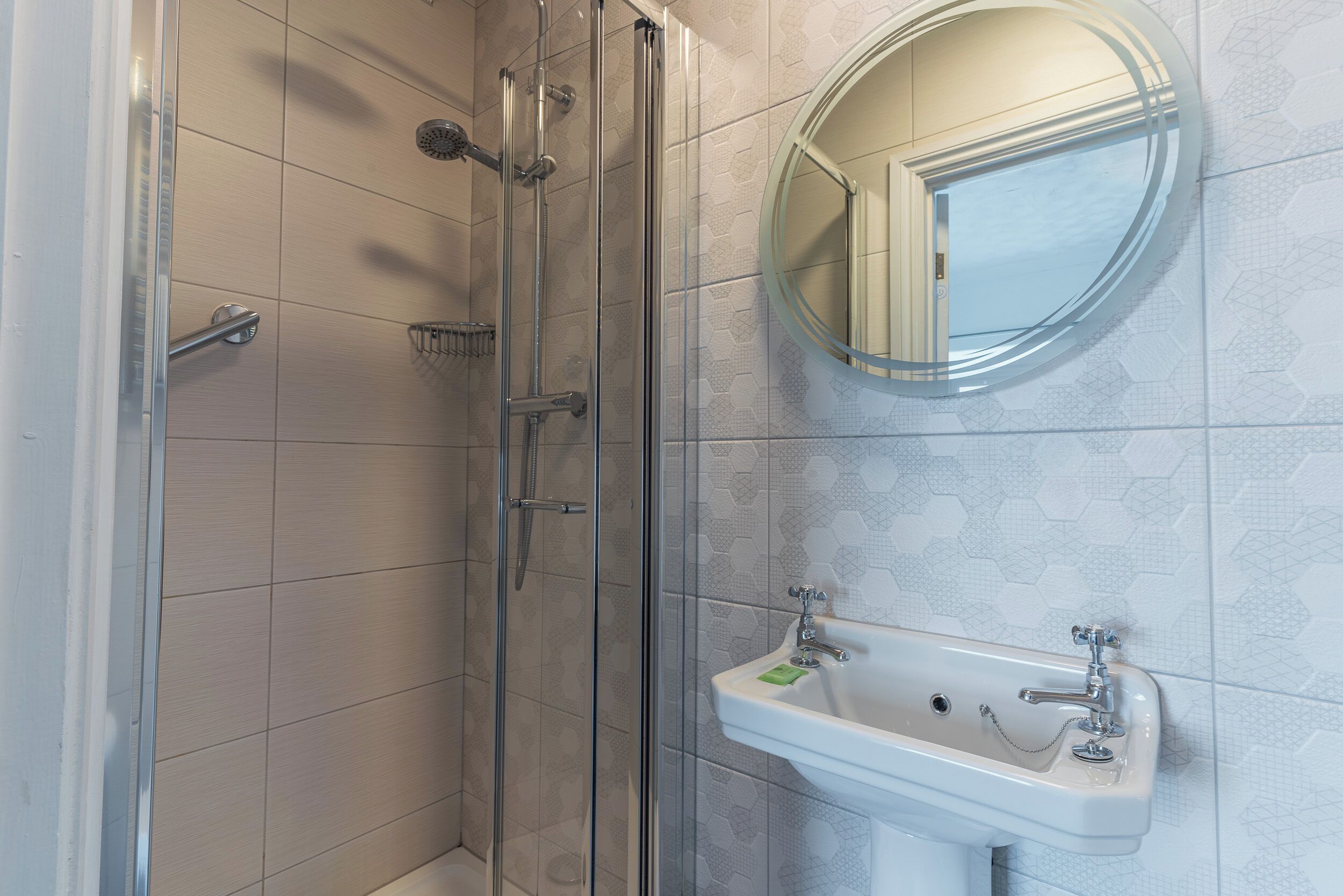 Une salle de bain avec une douche à parois de verre, un lavabo avec un miroir et des carreaux hexagonaux formant un motif.