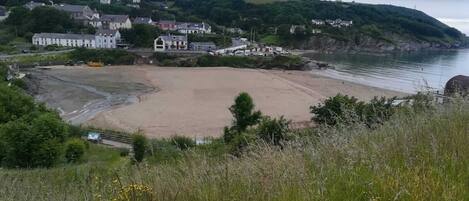 A coastal town with a sandy beach, houses, and a hill with greenery.