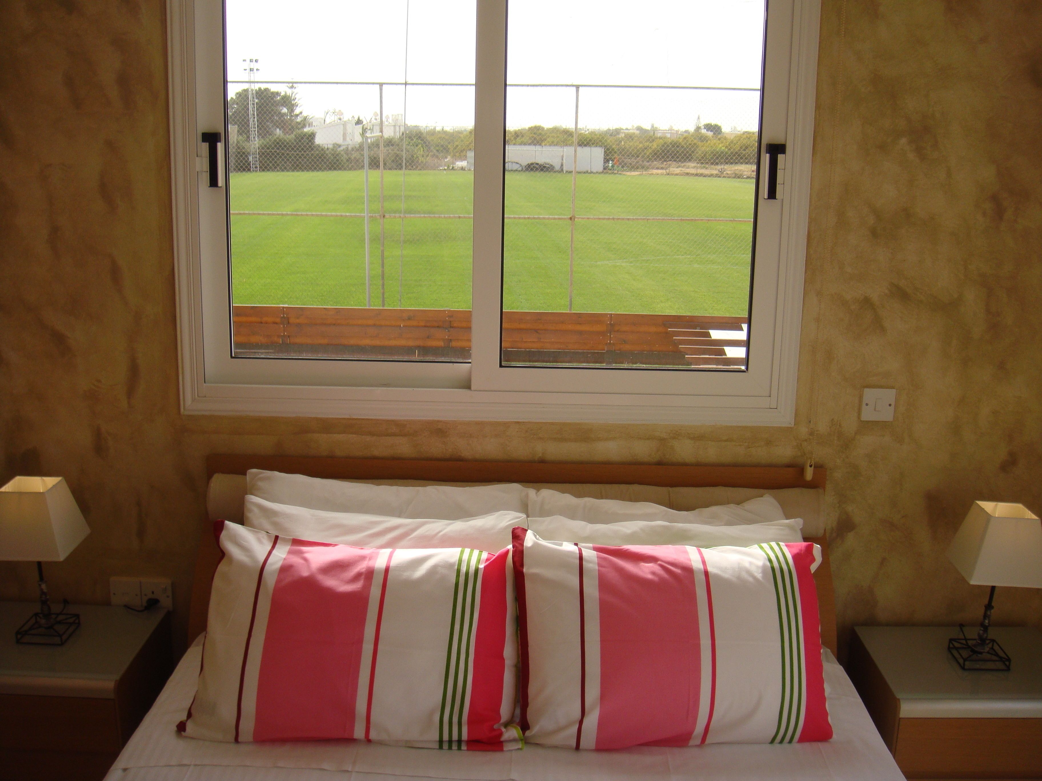 Habitación de hotel con cama, dos lámparas de noche y ventana con vistas a un campo verde.