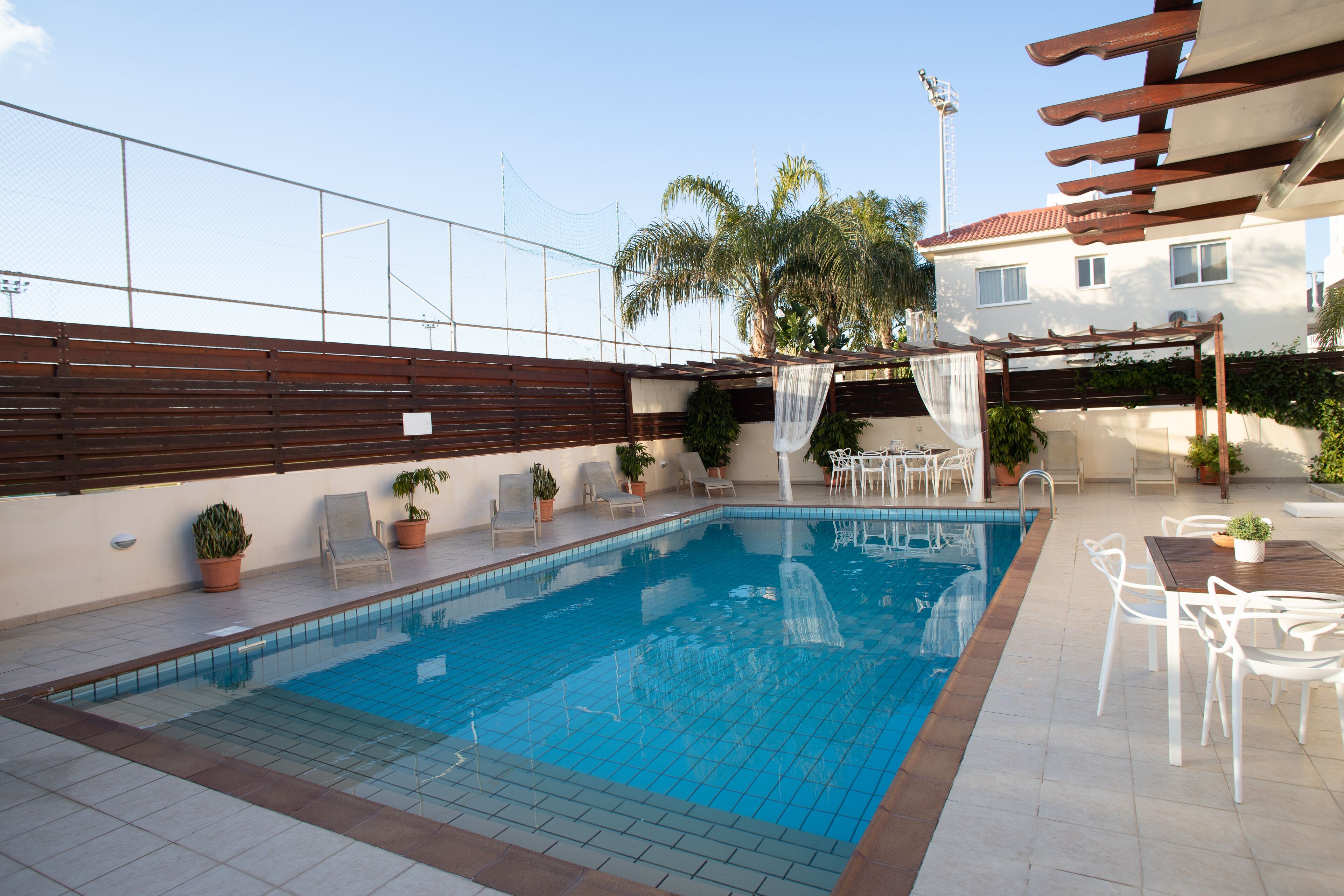 A swimming pool with tiled flooring, surrounded by potted plants and outdoor furniture.