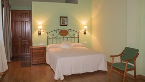 A bedroom with a bed, nightstands, a chair, and wooden cabinets. - CR La Flor del Naranjo (Cadalso)