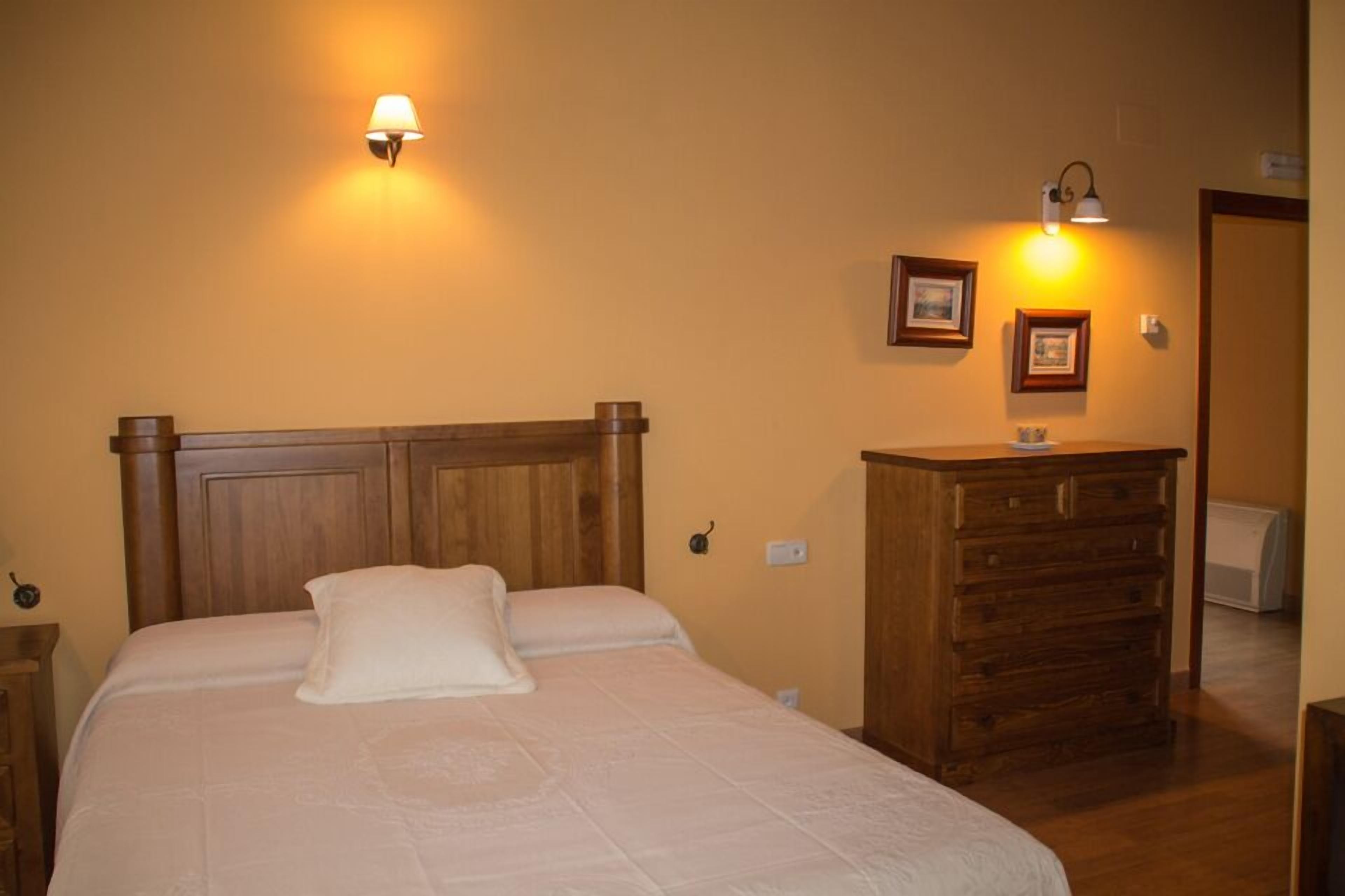 A bedroom with a wooden bed, a dresser, and wall-mounted lamps.