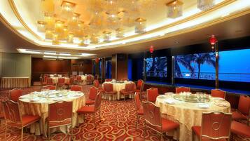Un salón de banquetes con mesas redondas, sillas rojas y suelo cubierto de alfombra roja.