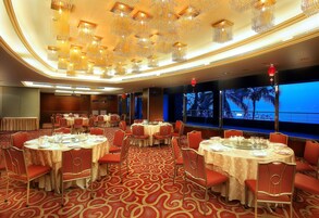 Un salón de banquetes con mesas redondas, sillas rojas y suelo cubierto de alfombra roja.