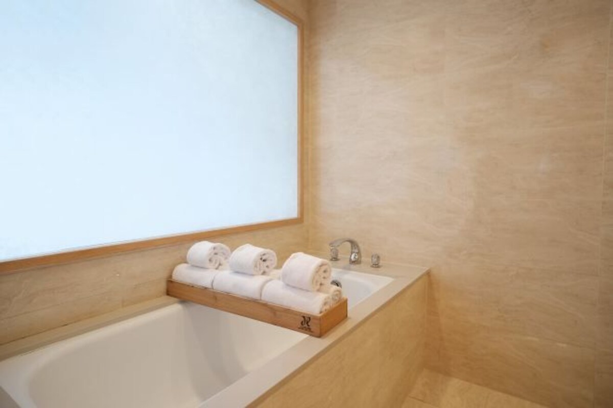 A bathroom with a bathtub, two sinks, and a wooden shelf holding rolled towels.
