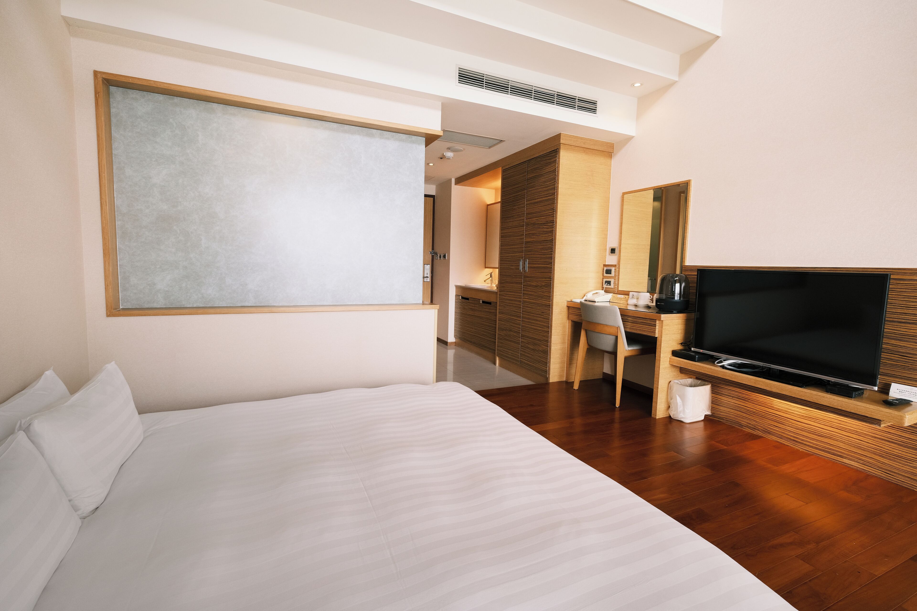 Una habitación de hotel moderna con una cama grande, un escritorio con televisor y un espejo.
