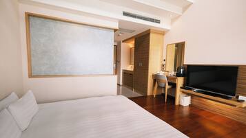 Una habitación de hotel moderna con una cama grande, un escritorio con televisor y un espejo.