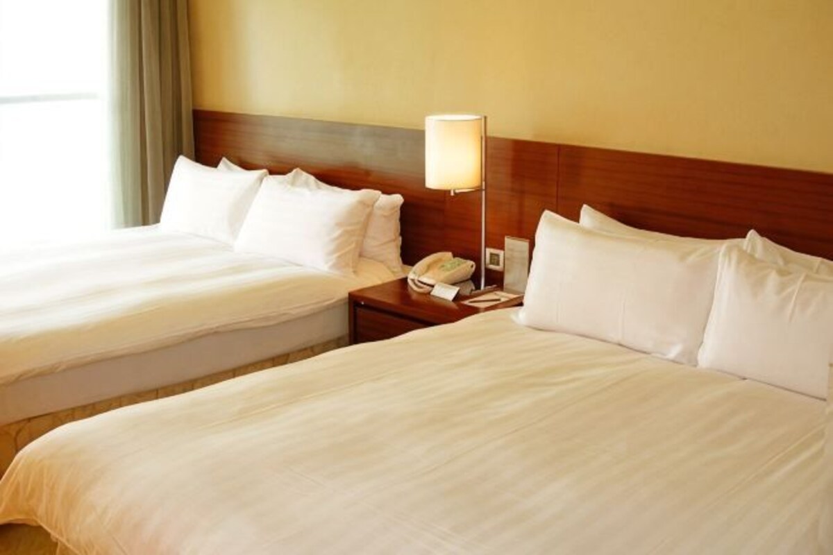 A hotel room with two beds, a bedside table with a lamp, and a phone.