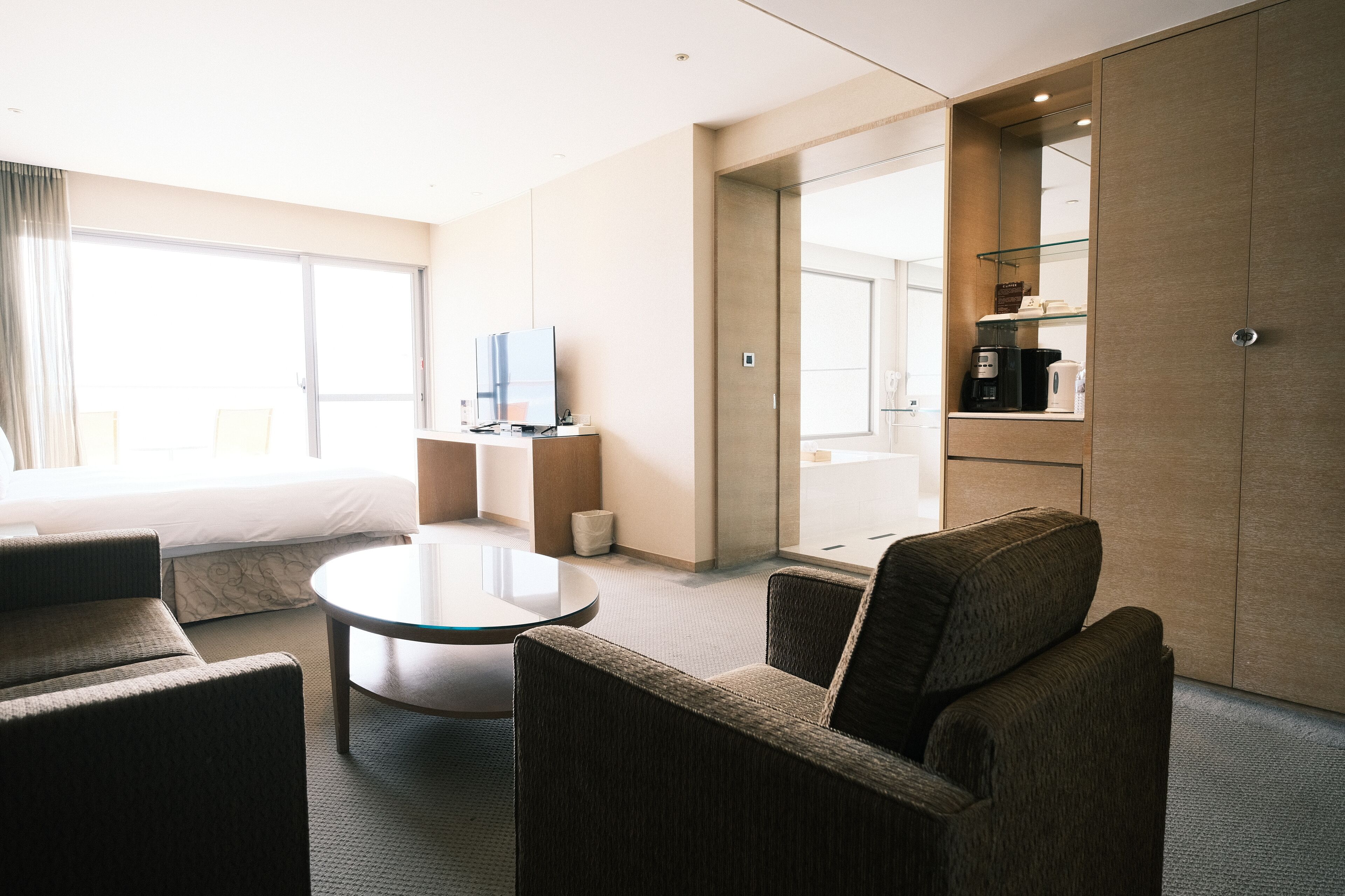 Una habitación de hotel moderna con cama, televisión, cafetera y zona de estar con mesa y sillas.