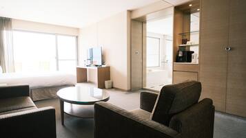 Una habitación de hotel moderna con cama, televisión, cafetera y zona de estar con mesa y sillas.