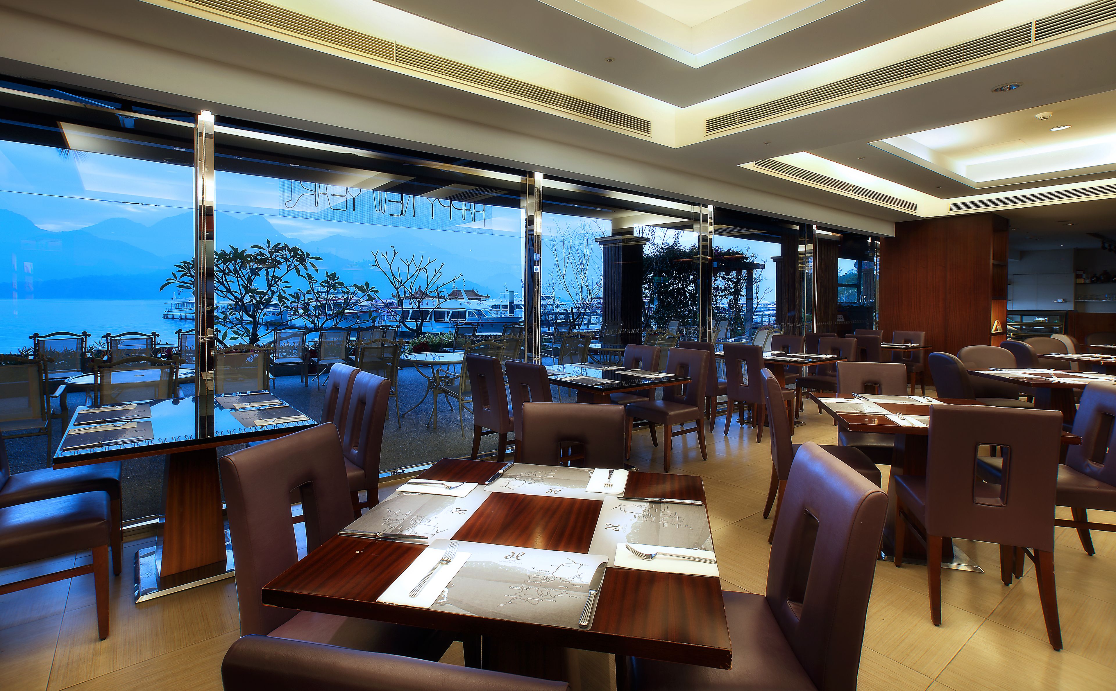 A restaurant with tables set for dining, large windows offering a view of the sea and boats, and a modern interior design.