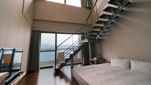 A bedroom with a large bed, a TV, a desk, and a staircase leading to a balcony with a view. - Hotel Del Lago (Yuchi)