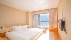 A hotel room with a large bed, a desk, a chair, and a view of the sea through a large window. - Hotel Del Lago (Yuchi)