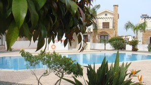 A swimming pool surrounded by greenery and a building with a stone facade. - Jolie Villa (Sotira)
