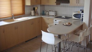 A kitchen with wooden cabinets, a sink, a toaster, a microwave, and a dining table with chairs. - Jolie Villa (Sotira)