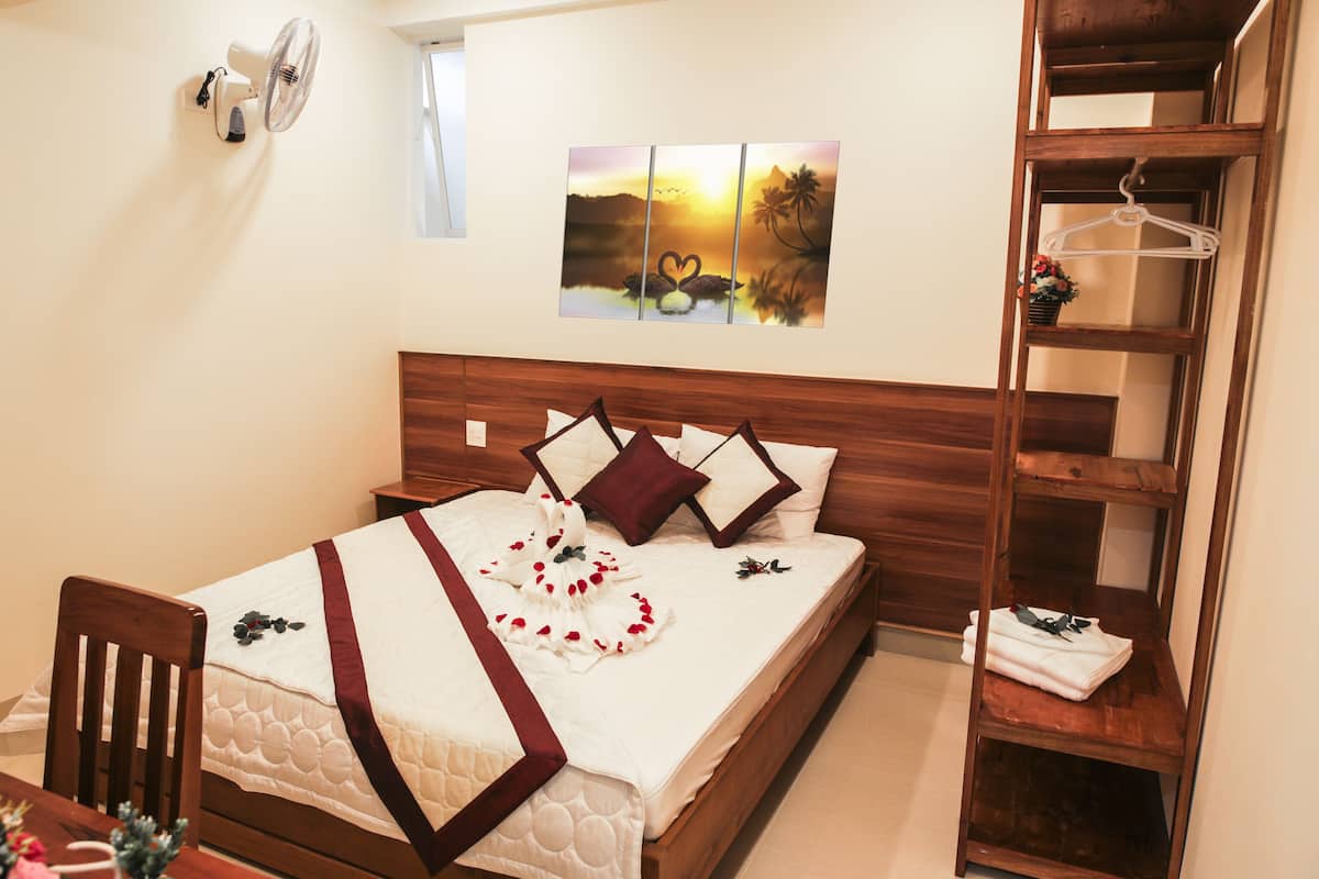 Ein ordentlich bezogenes Bett mit weißer und brauner Bettdecke, einem Holzkopfteil und einem Wandventilator.