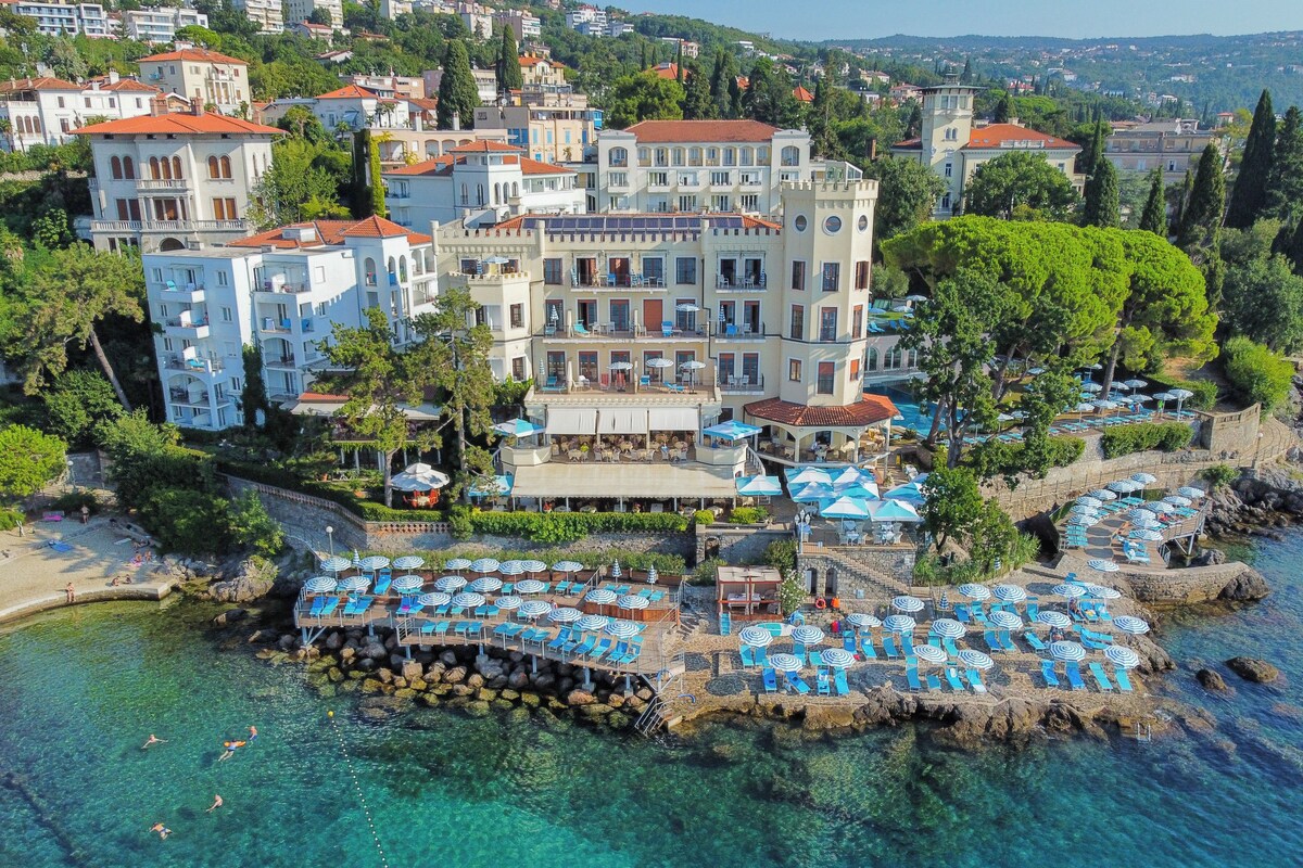 A coastal hotel with multiple balconies, a pool area, and a view of the sea.