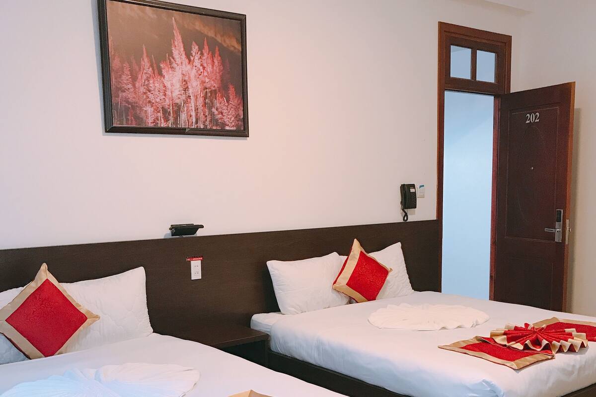 Two beds with white linens and red accents, a framed picture on the wall, and a door with the number 202.