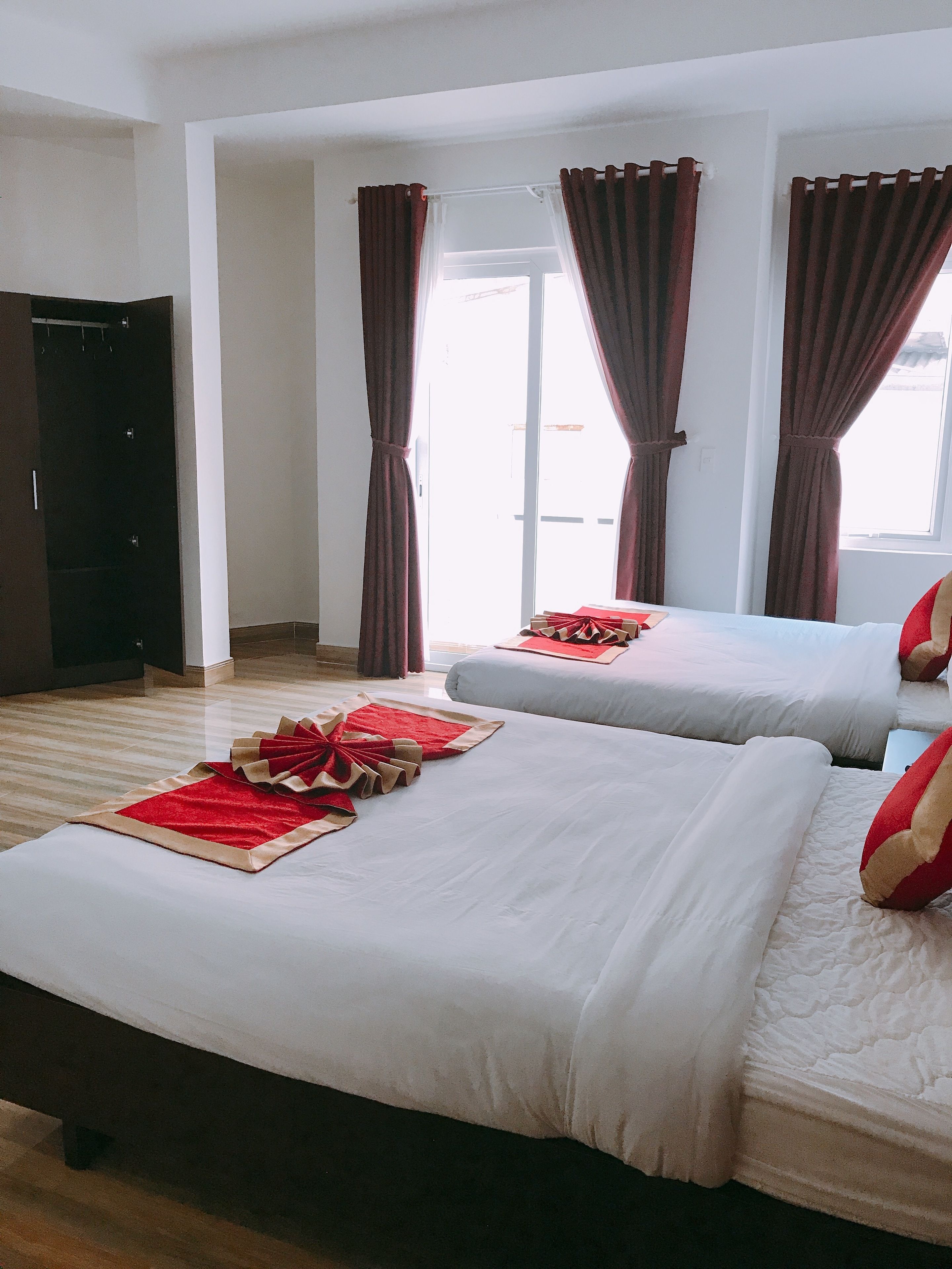A hotel room with two beds, a wardrobe, and a view of the outside.