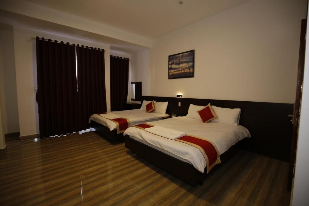 A hotel room with two beds, a large window with curtains, a painting on the wall, and a wooden floor.