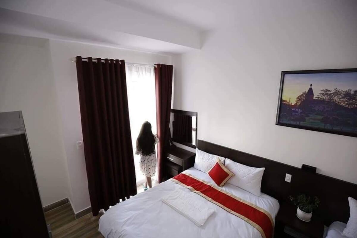A hotel room with a large bed, a TV, a desk, and a window with curtains.