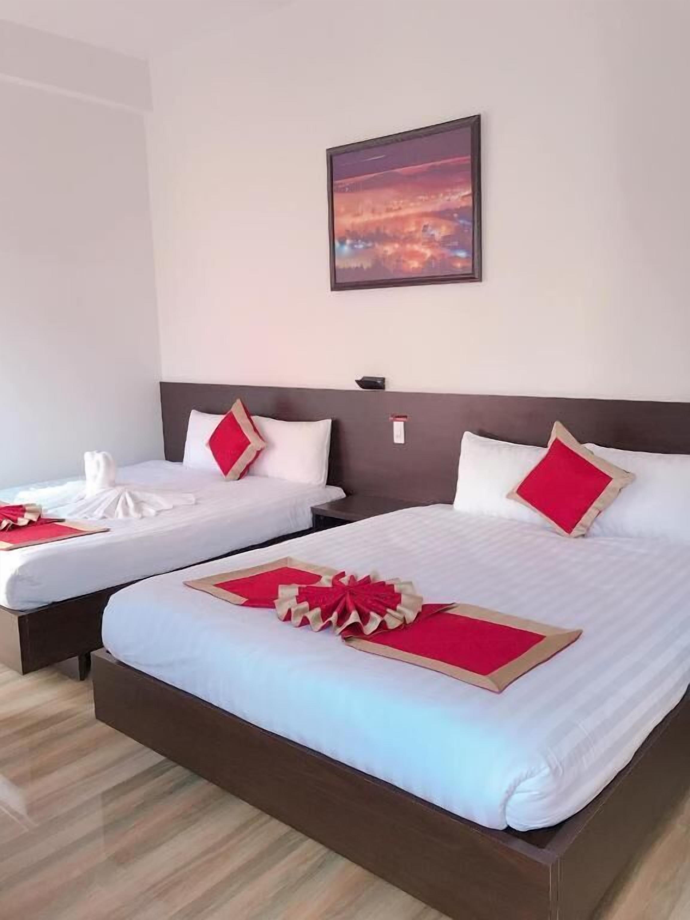 Ein Hotelzimmer mit zwei Betten, jeweils mit weißer Bettwäsche und roten Akzenten. Darüber an der Wand hängt ein gerahmtes Bild.