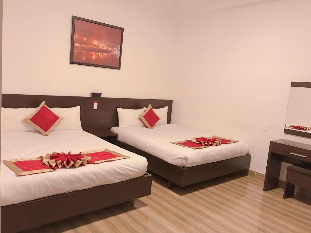 Hotelkamer met twee bedden, elk voorzien van witte beddengoed en rode accenten, een houten hoofdbord, een bureau met stoel, en een ingelijst schilderij aan de muur.