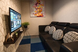 A modern living room with a flat-screen TV, a black leather sofa with patterned cushions, a blue and gray checkered rug, and a large abstract painting on the wall. - Vibrant Hostel (Kota Kinabalu)