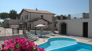 A pool area with a building, outdoor seating, and a clear sky. - Borgo Valmarina (Follonica)