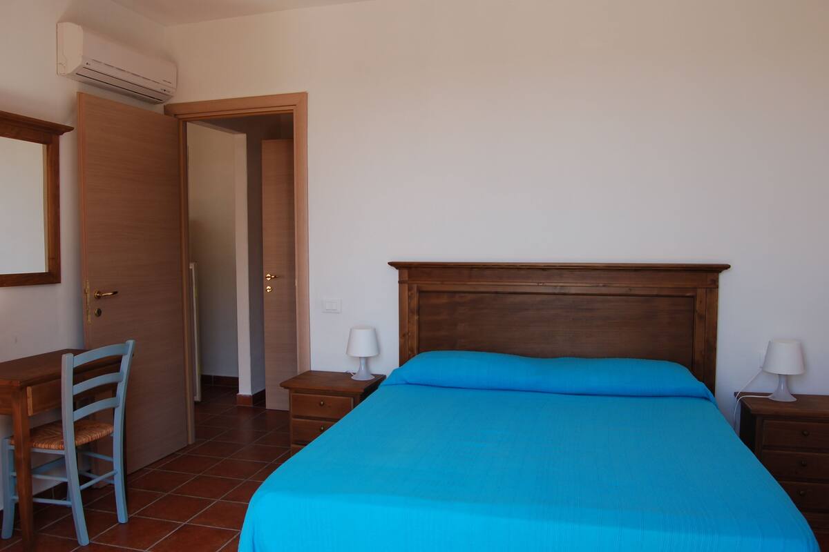 A bedroom with a wooden bed, two bedside tables with lamps, a wooden chair, and a wardrobe.