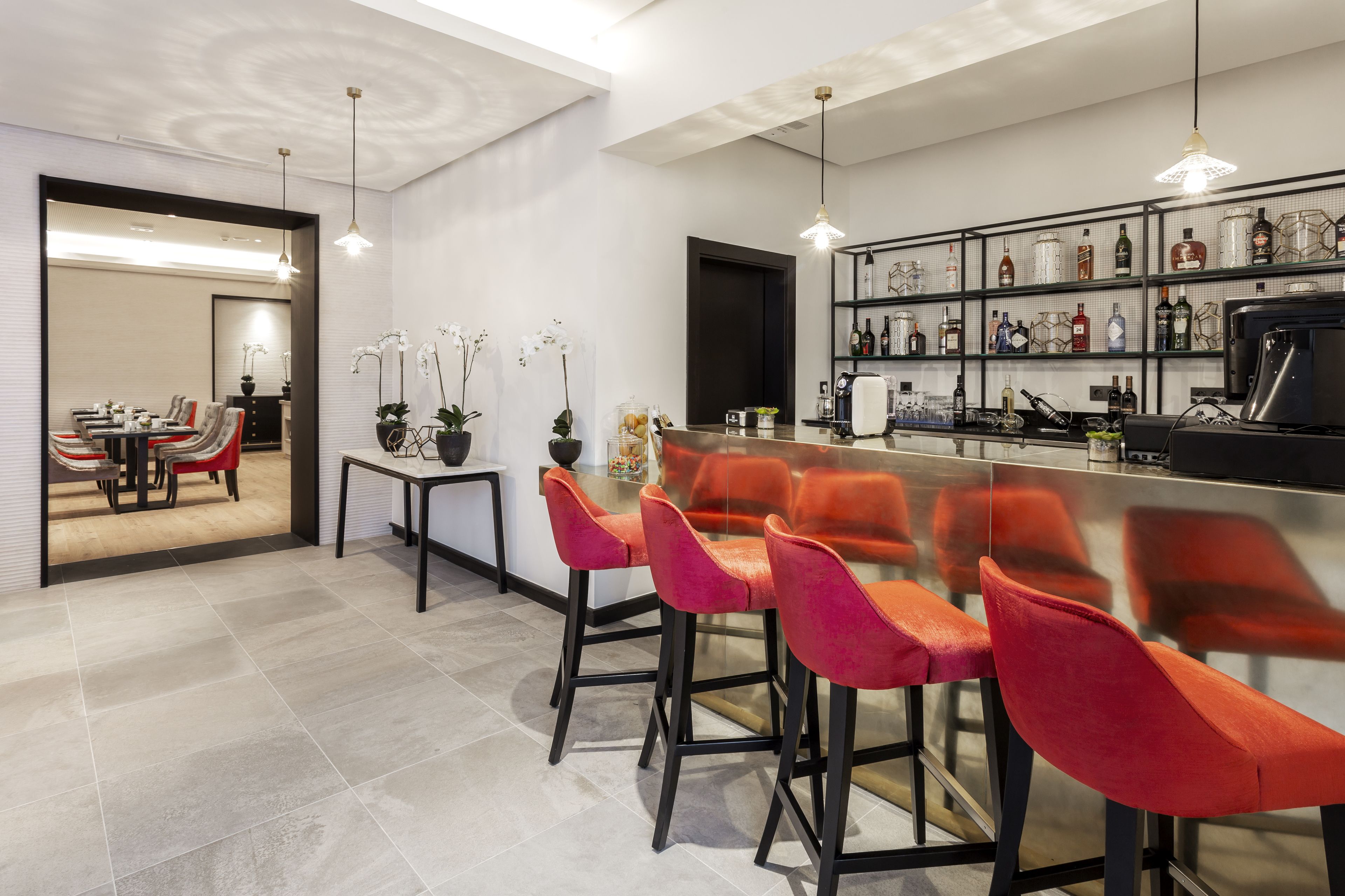 A modern kitchen with a bar area, red bar stools, and a wine rack with various bottles.