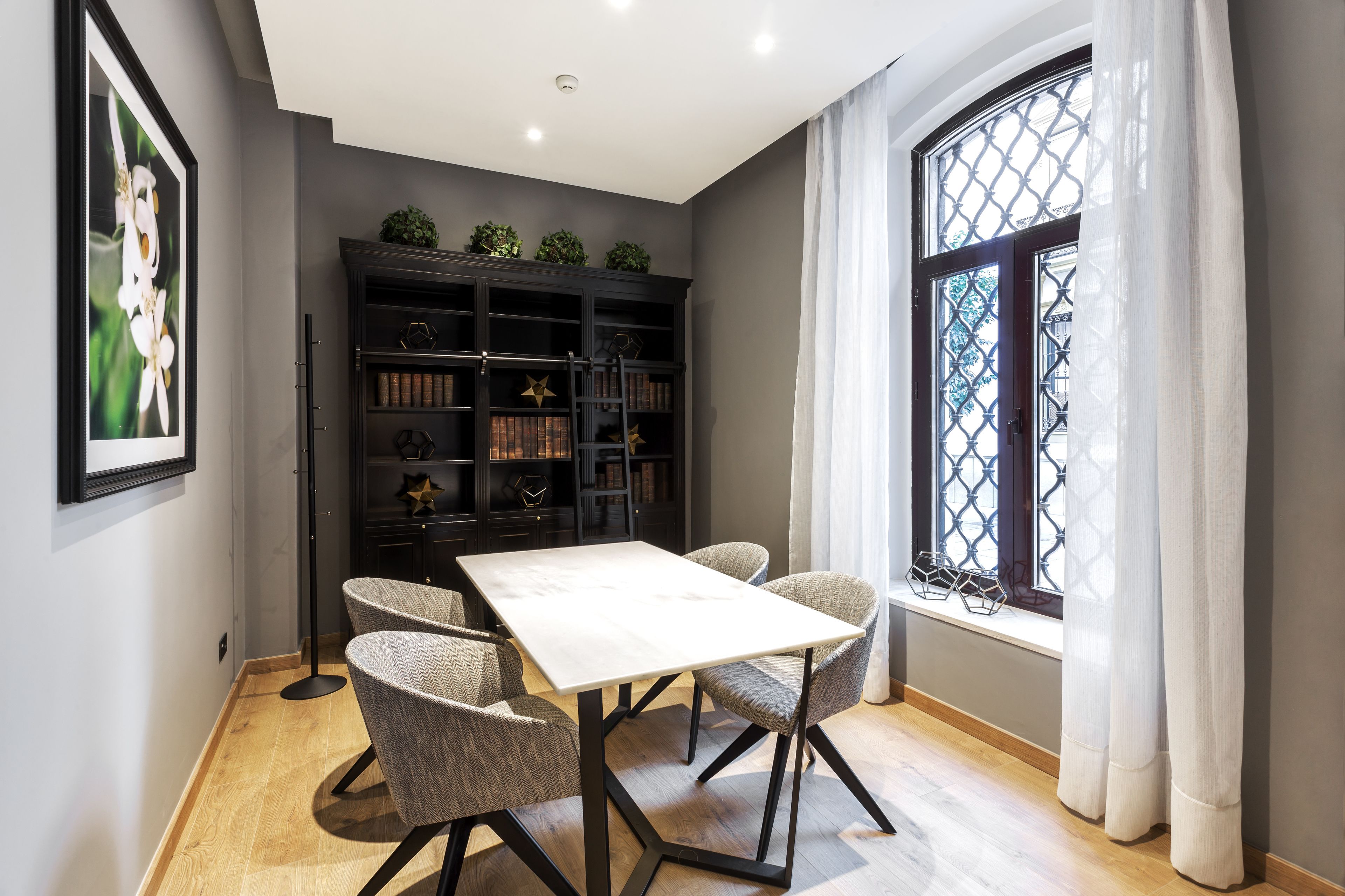 A dining area with a table and chairs, a bookshelf, and a window with curtains.