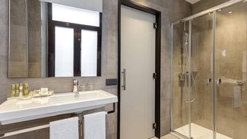 Un baño moderno con un espejo grande, un lavabo blanco y una cabina de ducha de vidrio.